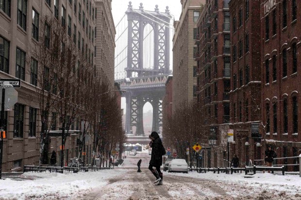 The Manhattan Bridge is seen in the background as commuters make their way through the streets of Dumbo after a snow storm in New York